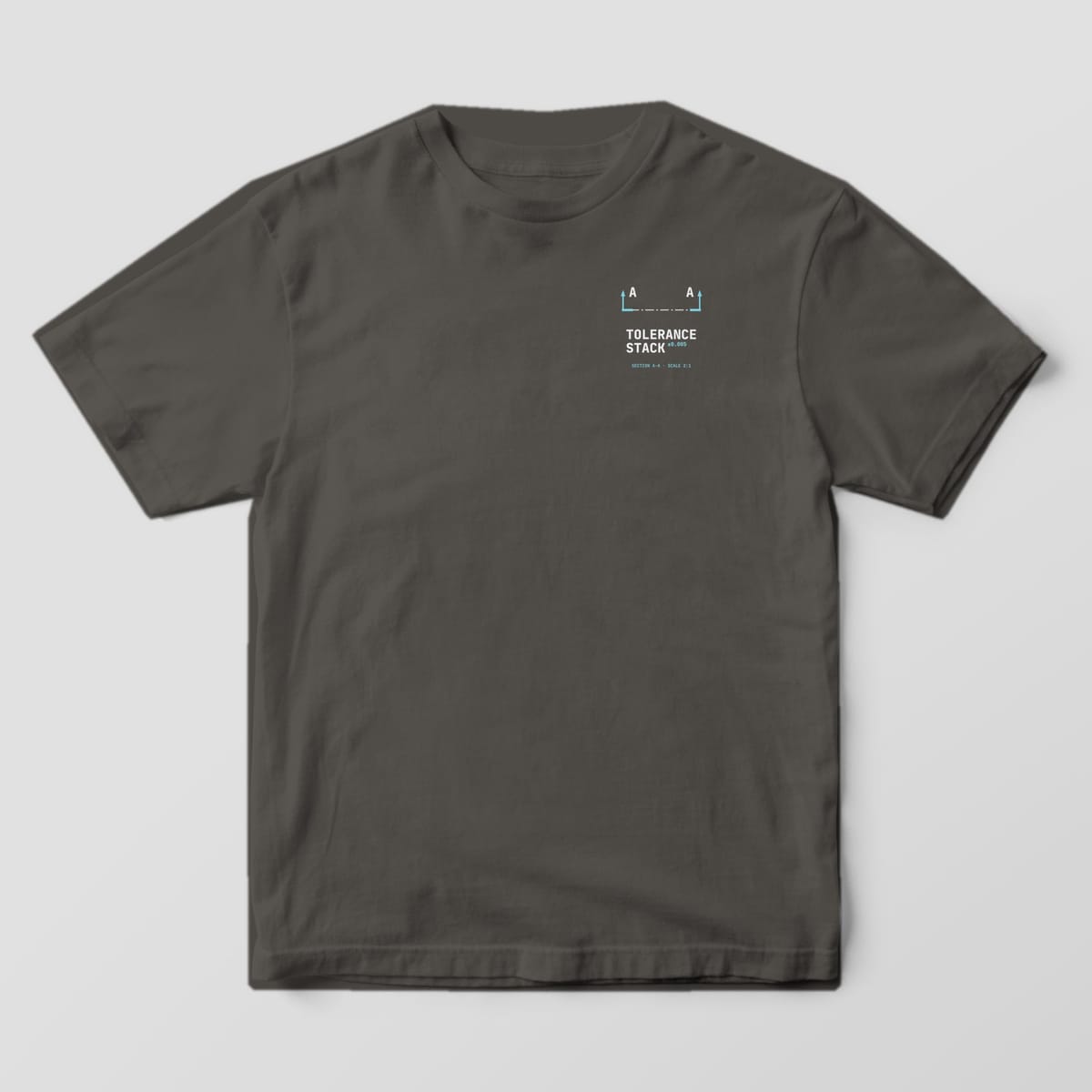 Front of a Pepper Comfort Colors 1717 tee with a small left-chest cutting-plane symbol with A arrows above the words Tolerance Stack.