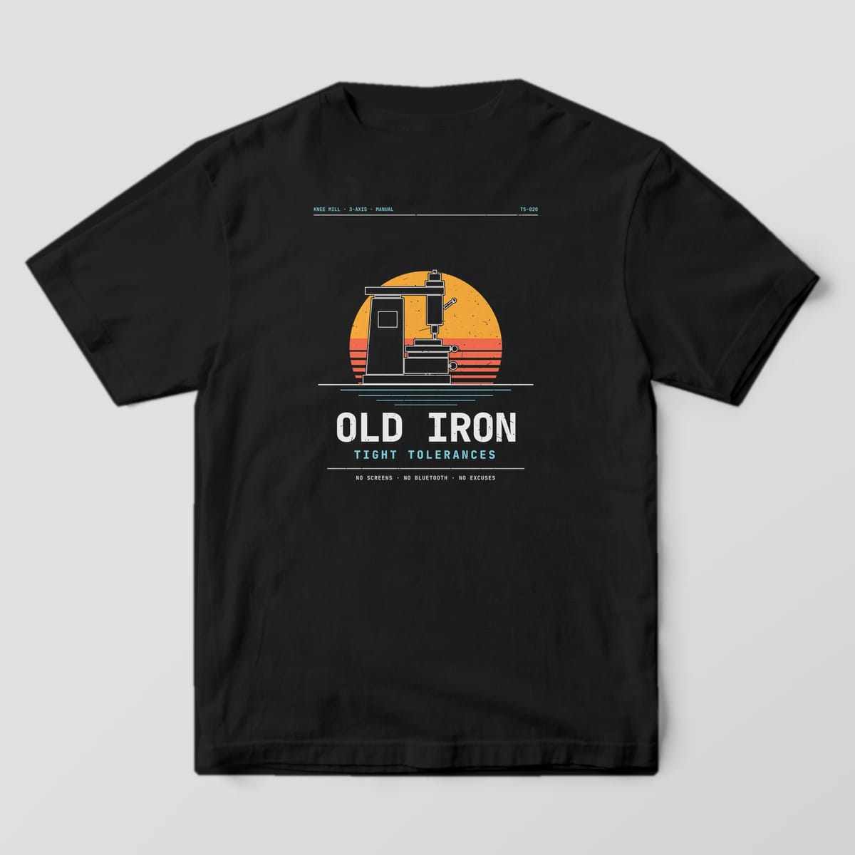 Back of a Black Comfort Colors 1717 tee with an amber and orange striped sunset behind a knee mill silhouette and the words Old Iron, Tight Tolerances.