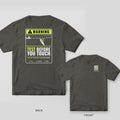 Back and front of a pepper Test Before You Touch warning-sign lineman T-shirt shown together, back print large on the left and the small chest print on the right