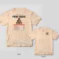 Print Queue 3D printing shirt shown back and front on Ivory Comfort Colors 1717: "It's Not a Hobby, It's a Print Queue" over a pyramid of six orange and charcoal spools, with a seven-item Now Printing queue list and print times