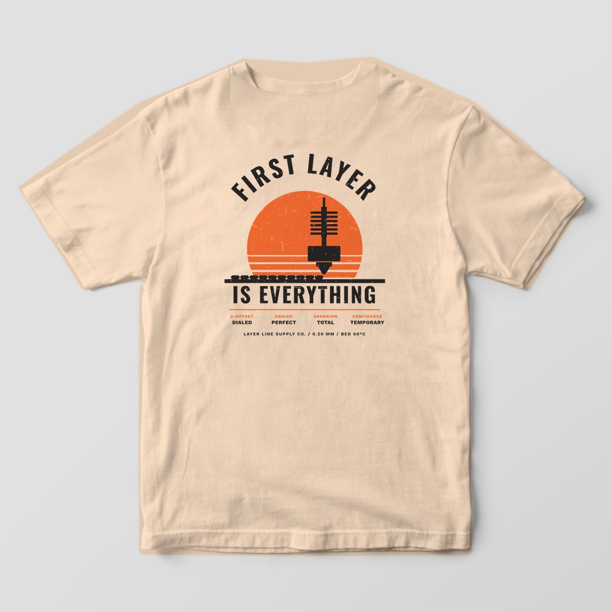 Back print on an Ivory Comfort Colors 1717 tee: Arched "First Layer" over a striped orange sunset and nozzle laying down a perfect first layer, "Is Everything" below, with a spec row: Z-offset dialed, squish perfect, adhesion total, confidence…