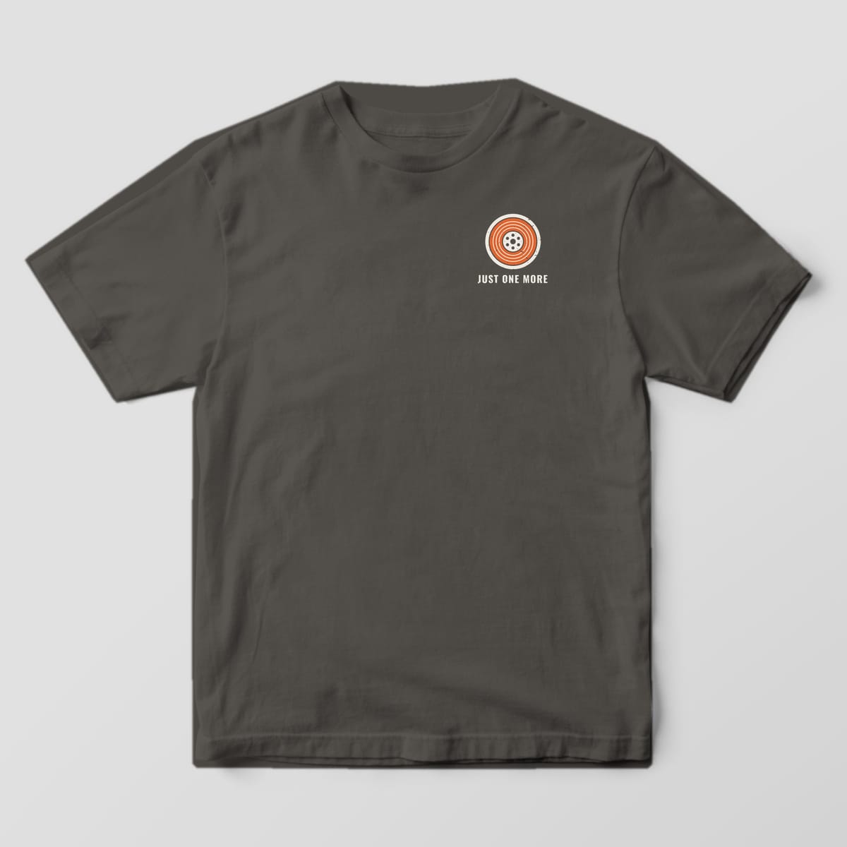 Front of the Pepper Comfort Colors 1717 tee showing the left-chest print: Small left-chest orange and off-white filament spool with "Just One More" below