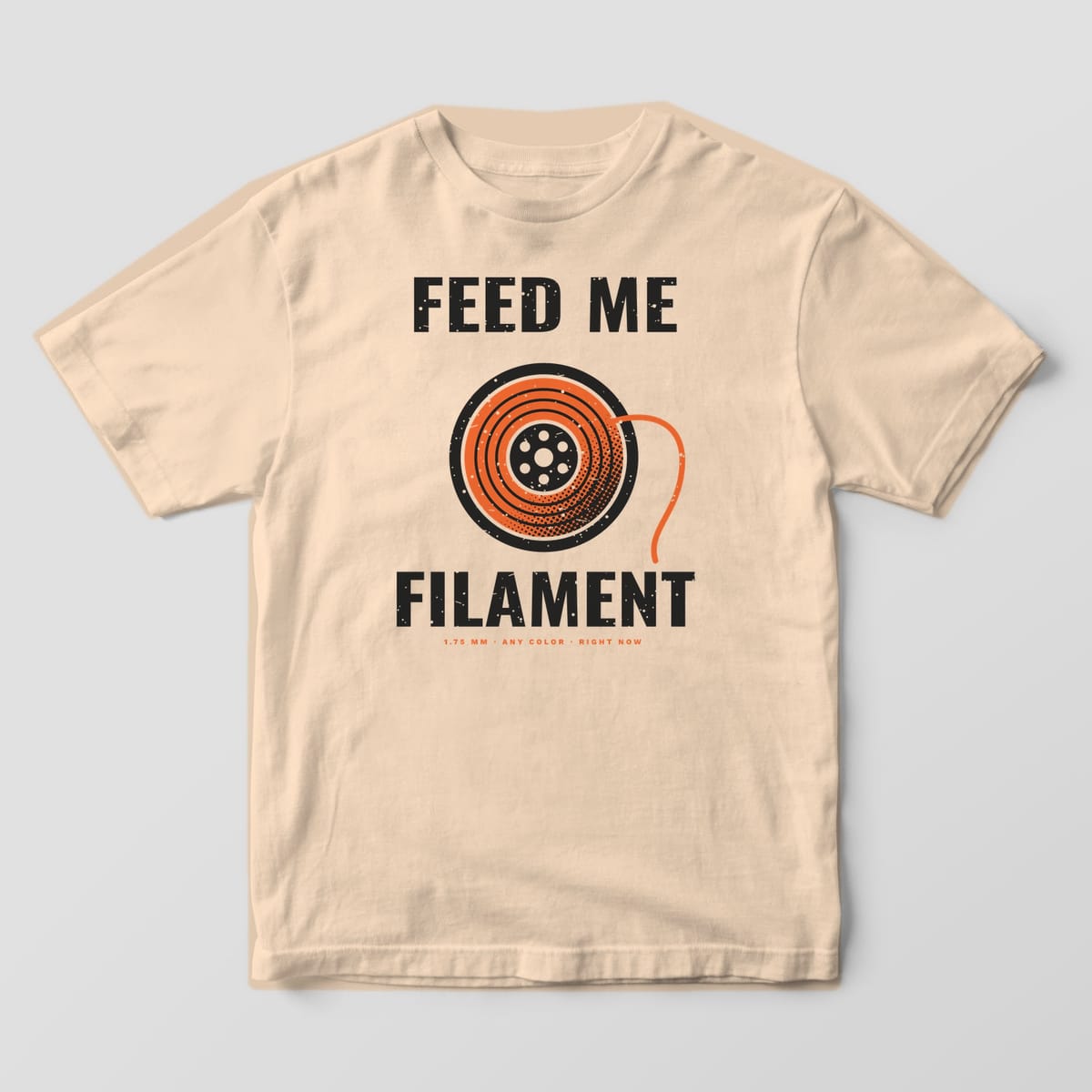 Front of the Ivory Comfort Colors 1717 tee showing the full-front print: Full-front print: "Feed Me Filament" around a large orange halftone filament spool, with "1.75 mm · Any Color · Right Now"