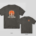 Still Printing Retro Sunset 3D printing shirt shown back and front on Pepper Comfort Colors 1717: "Overnight Shift" over a striped orange sunset framed by a printer gantry with a half-printed vase, "Still Printing" in bold below