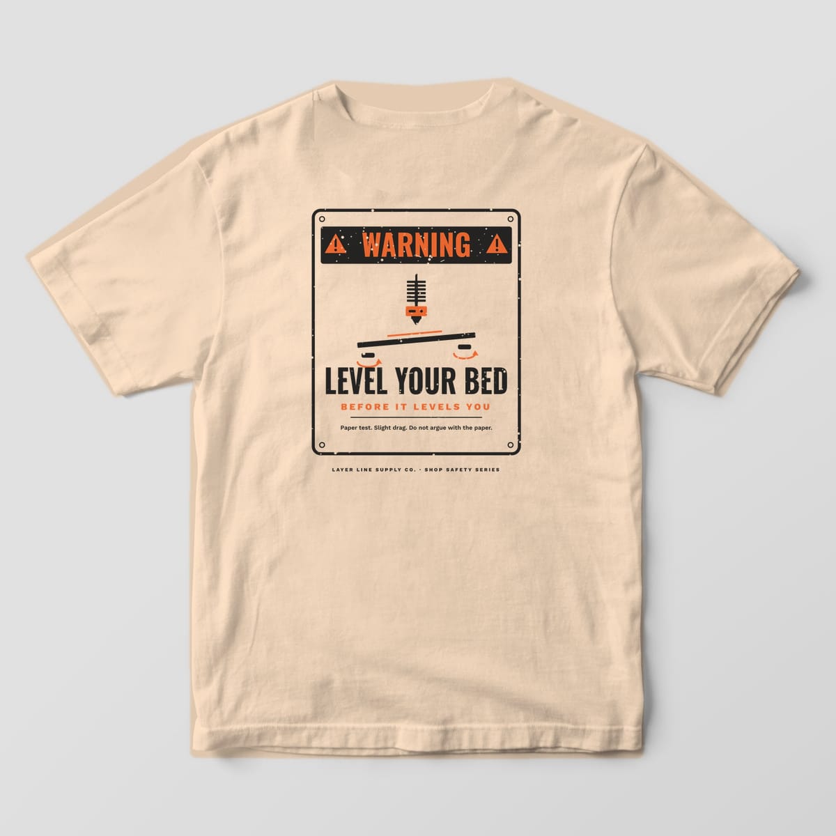 Back print on an Ivory Comfort Colors 1717 tee: Distressed warning sign: "Warning" header, nozzle over a tilted print bed with knobs, "Level Your Bed, Before It Levels You" and "Paper test. Slight drag. Do not argue with the paper."