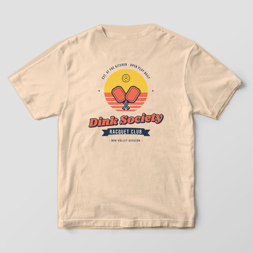Back print on an Ivory Comfort Colors 1717 tee: Dink Society Racquet Club badge with crossed coral paddles over a striped yellow sunset