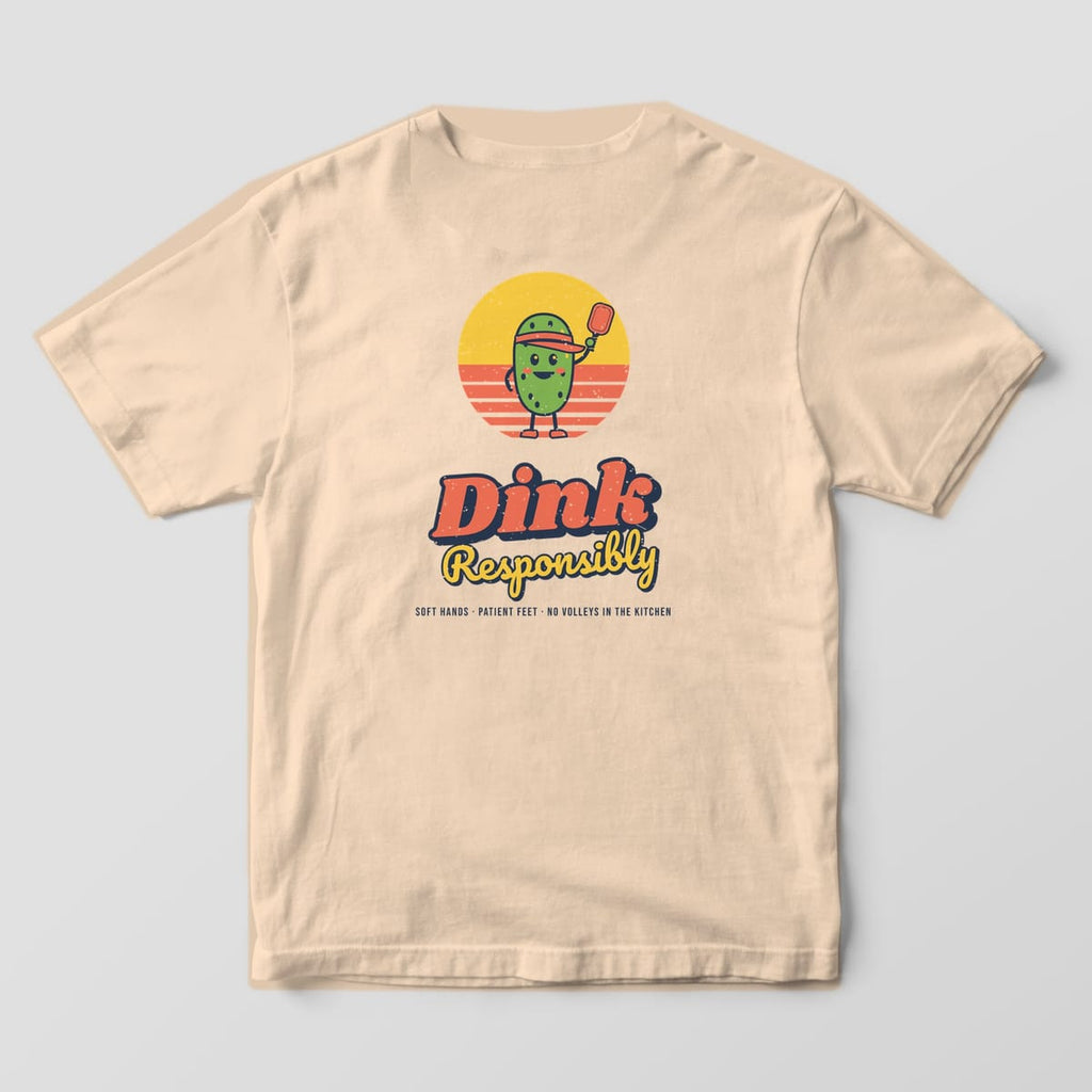 Back print on an Ivory Comfort Colors 1717 tee: Smiling green pickle in a coral visor holding a paddle over a striped sunset with Dink Responsibly script