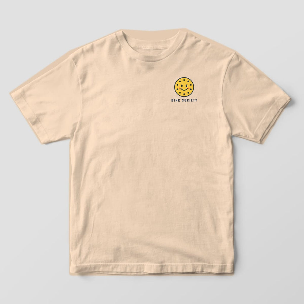 Front of the Ivory Comfort Colors 1717 tee showing the left-chest print: Left-chest smiling yellow pickleball with rosy cheeks over "Dink Society"