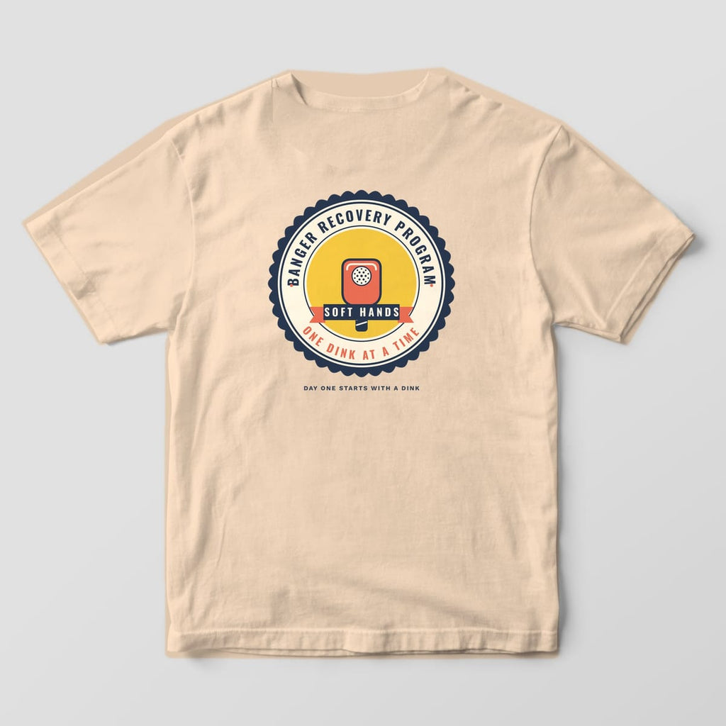 Back print on an Ivory Comfort Colors 1717 tee: Scalloped Banger Recovery Program seal with a coral paddle, Soft Hands ribbon and One Dink at a Time