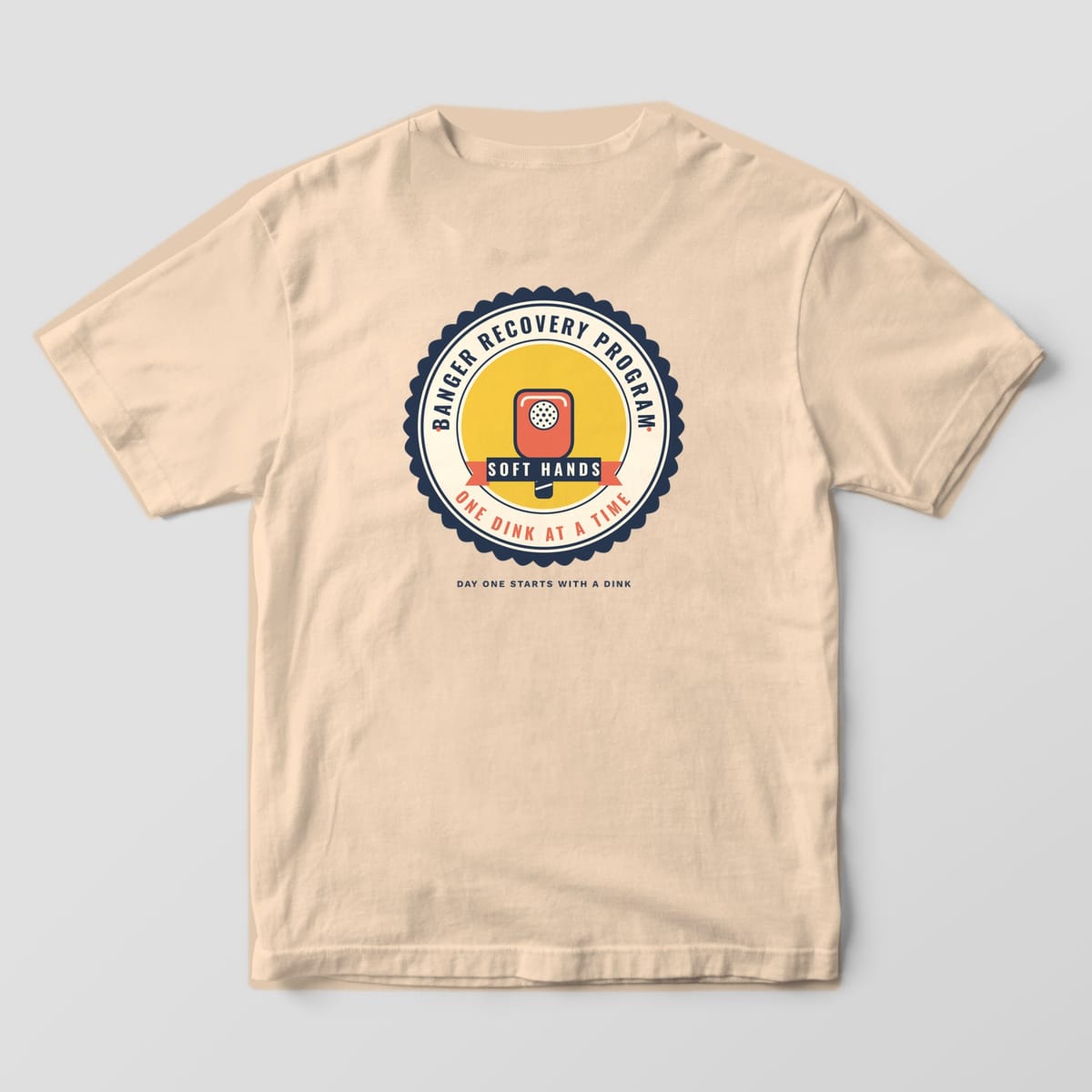 Back print on an Ivory Comfort Colors 1717 tee: Scalloped Banger Recovery Program seal with a coral paddle, Soft Hands ribbon and One Dink at a Time