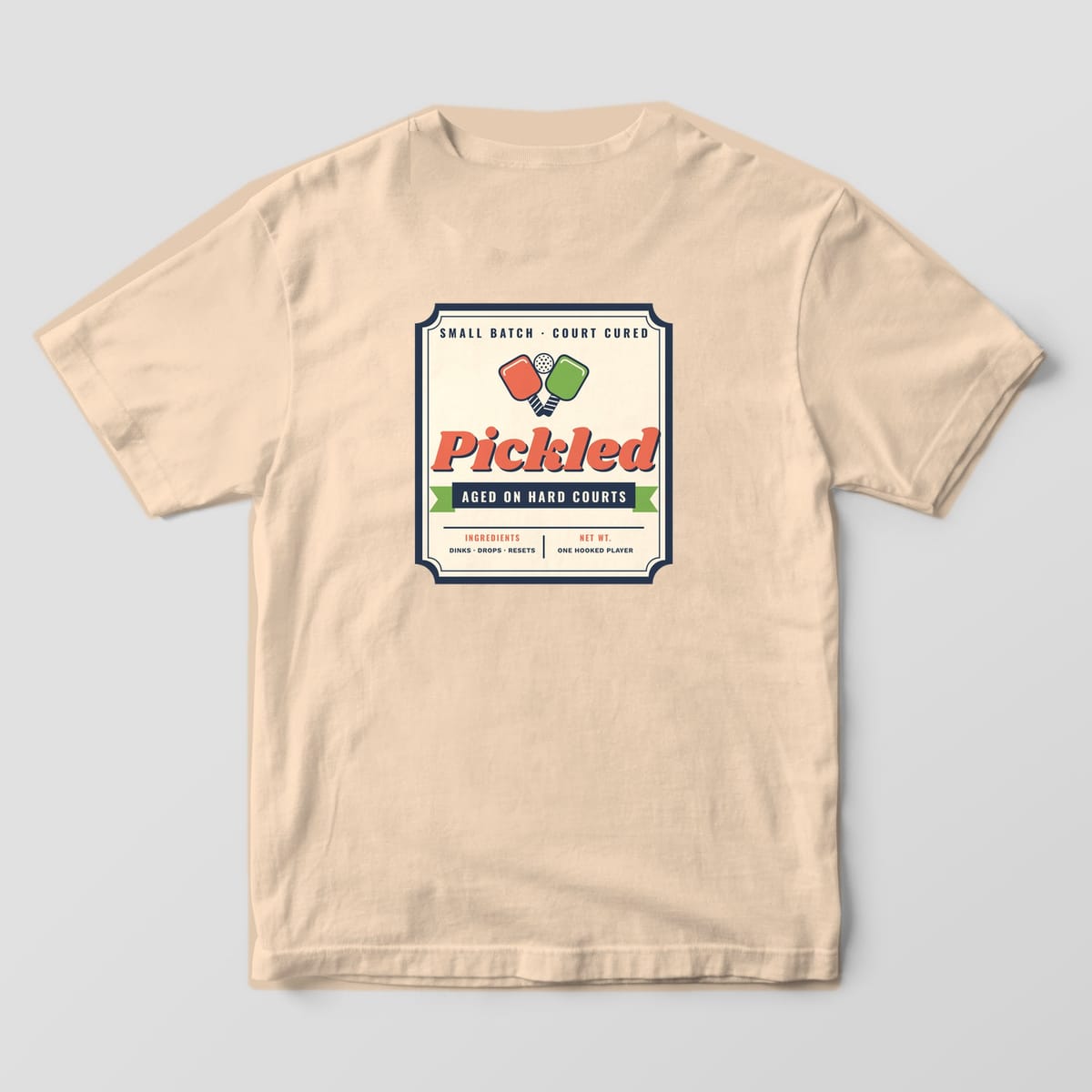 Back print on an Ivory Comfort Colors 1717 tee: Vintage pickle jar label reading Pickled, Aged on Hard Courts with crossed coral and green paddles