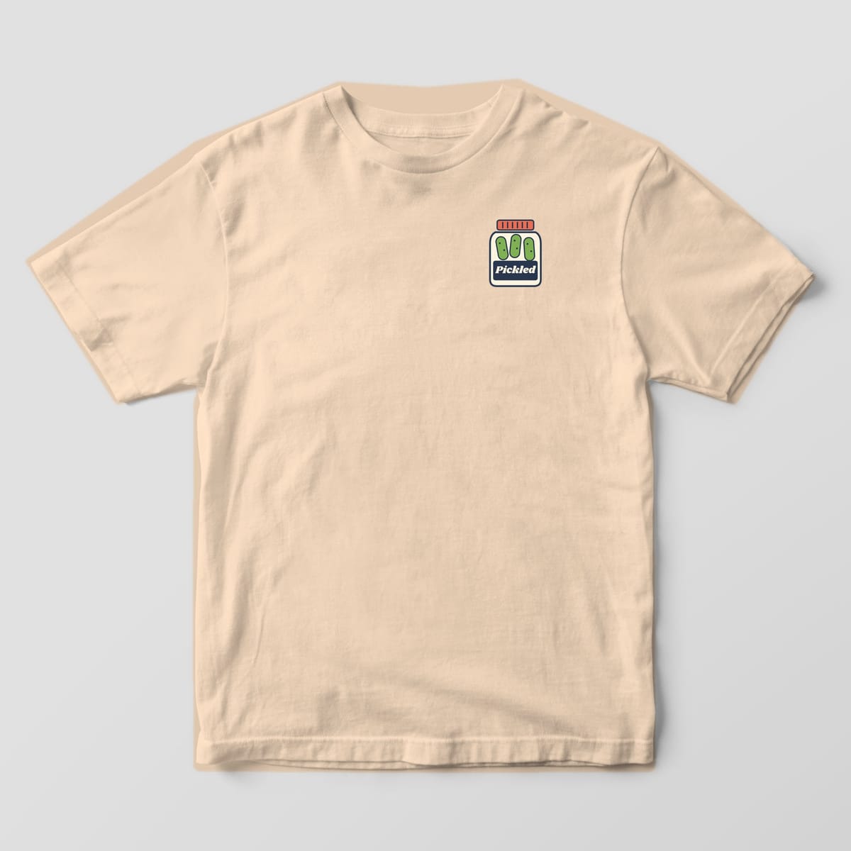 Front of the Ivory Comfort Colors 1717 tee showing the left-chest print: Left-chest pickle jar with three green pickles and a navy "Pickled" label