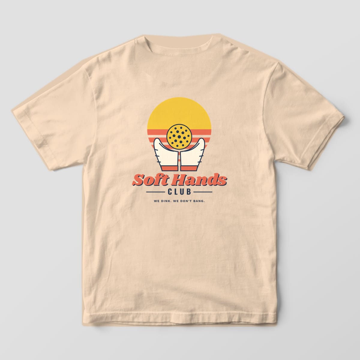 Back print on an Ivory Comfort Colors 1717 tee: Two hands cradling a yellow pickleball in front of a striped sunset over Soft Hands Club script