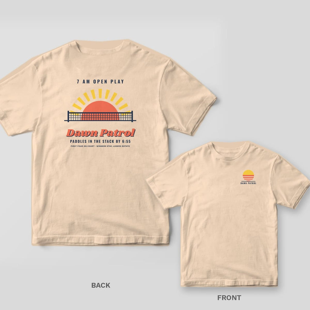 Dawn Patrol pickleball shirt shown back and front on Ivory Comfort Colors 1717: Coral sun rising behind a navy pickleball net with yellow rays and Dawn Patrol script