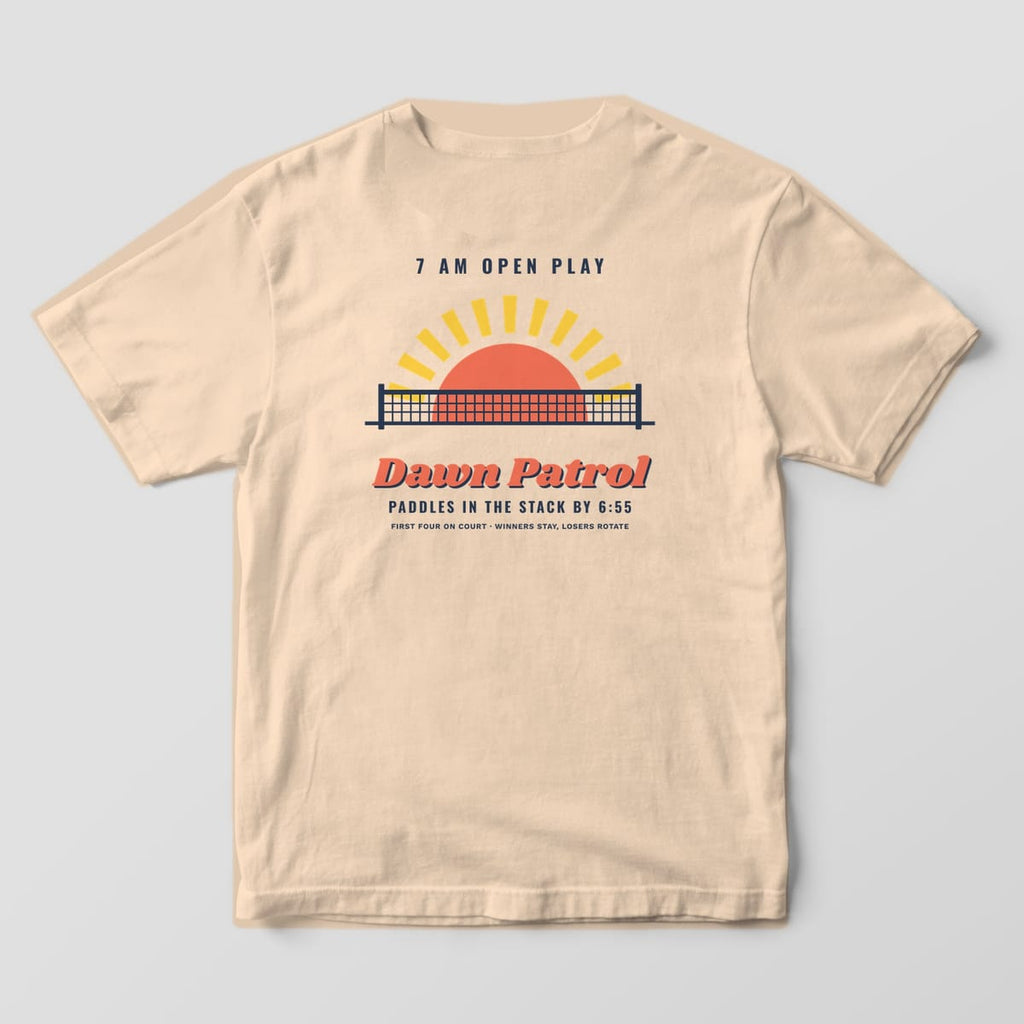 Back print on an Ivory Comfort Colors 1717 tee: Coral sun rising behind a navy pickleball net with yellow rays and Dawn Patrol script