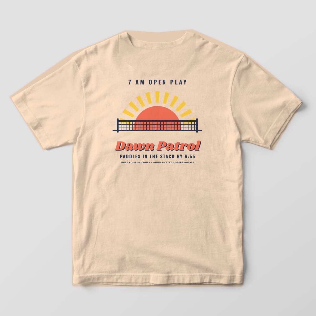 Back print on an Ivory Comfort Colors 1717 tee: Coral sun rising behind a navy pickleball net with yellow rays and Dawn Patrol script
