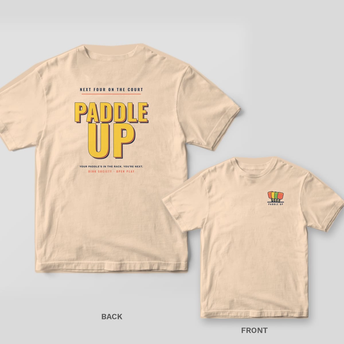 Paddle Up pickleball shirt shown back and front on Ivory Comfort Colors 1717: Stacked yellow block letters reading Paddle Up with coral and navy shadows