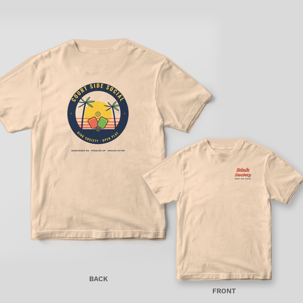 Court Side Social pickleball shirt shown back and front on Ivory Comfort Colors 1717: Round tropical badge with palm trees, crossed paddles and a yellow sun ringed by Court Side Social