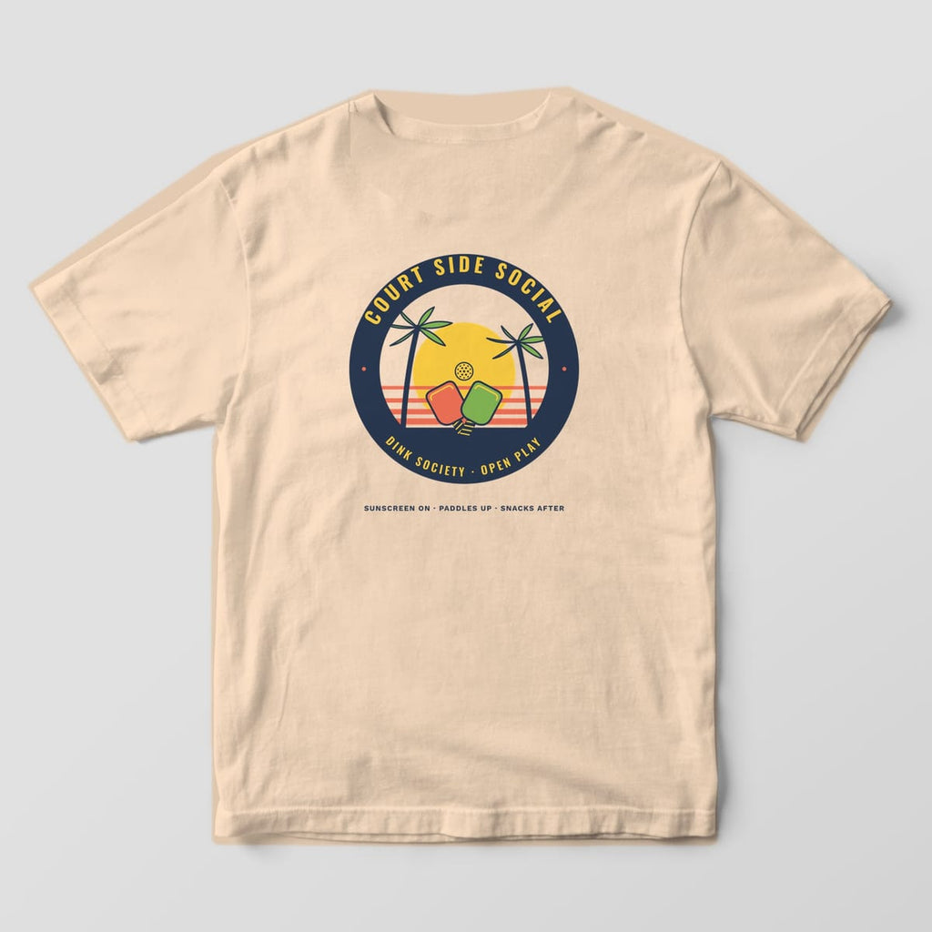 Back print on an Ivory Comfort Colors 1717 tee: Round tropical badge with palm trees, crossed paddles and a yellow sun ringed by Court Side Social