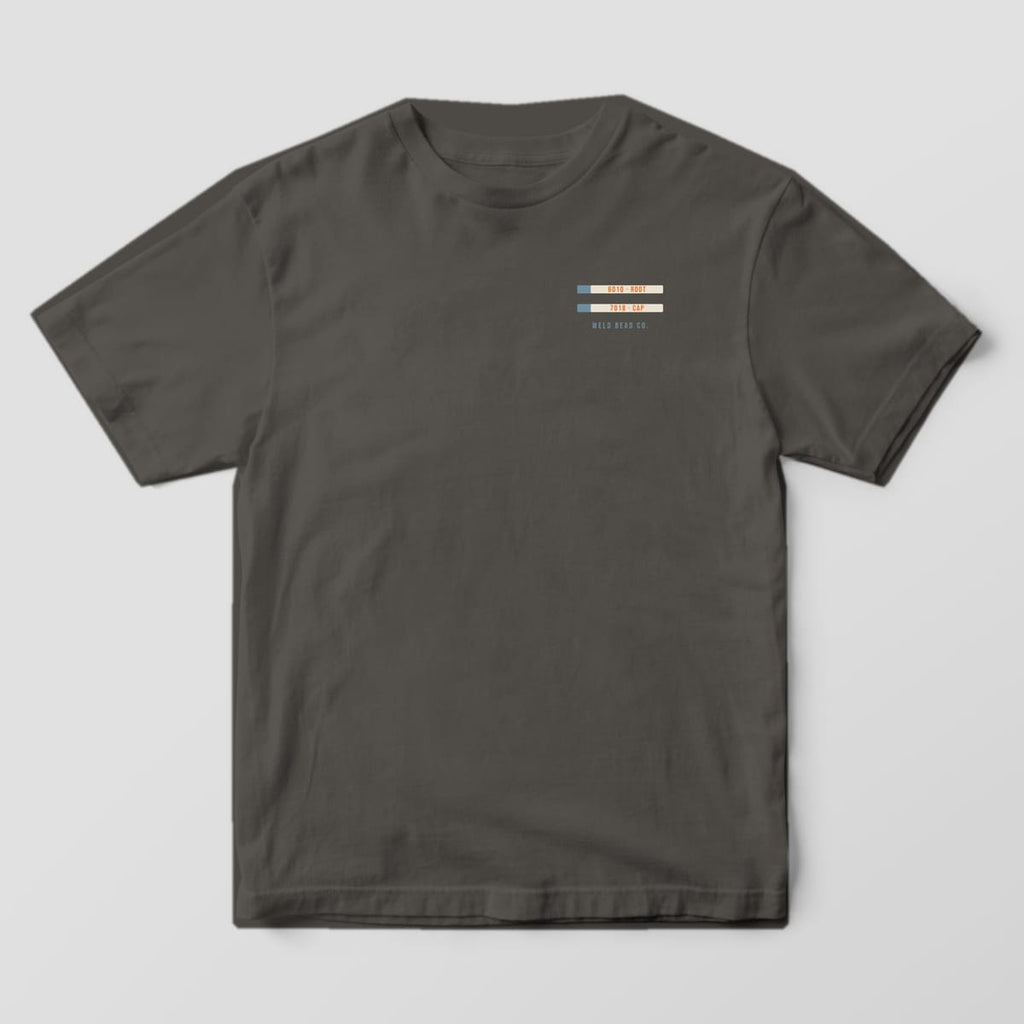 Front of the Pepper Comfort Colors 1717 tee showing the left-chest print: Small left-chest pair of electrode labels, "6010 · Root" and "7018 · Cap", over "Weld Bead Co."