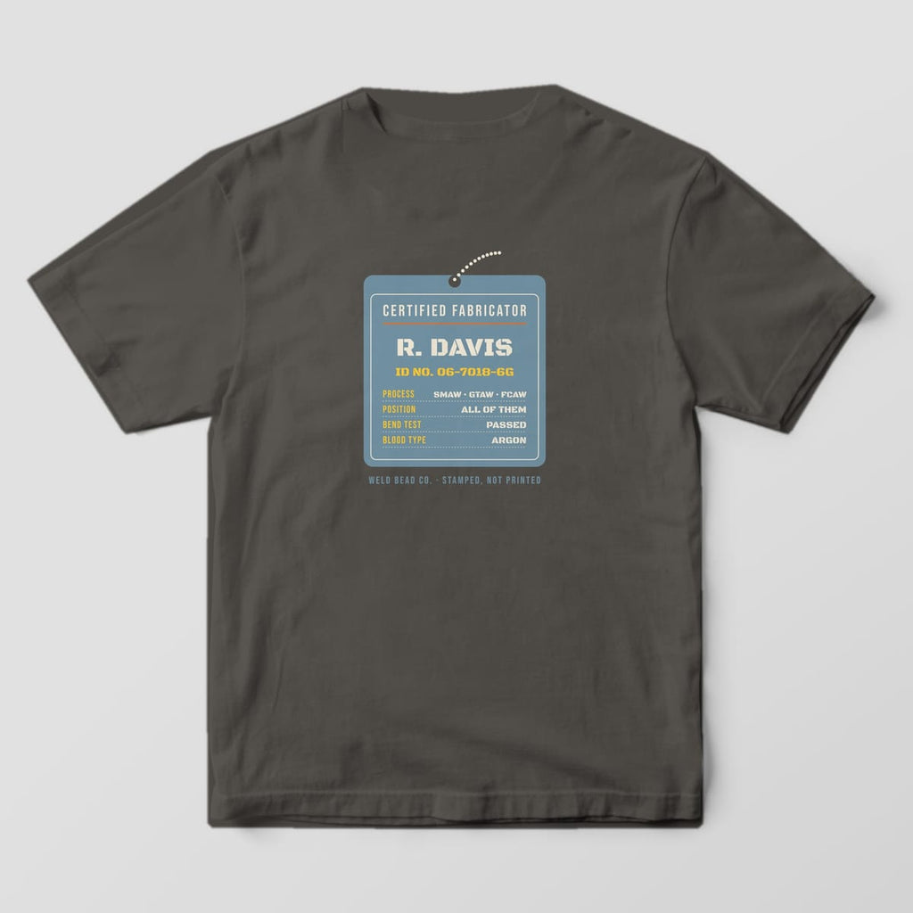 Back print on a Pepper Comfort Colors 1717 tee: A hanging steel ID tag: "Certified Fabricator", the custom name, ID number and a spec list (process, position, bend test, blood type: argon)