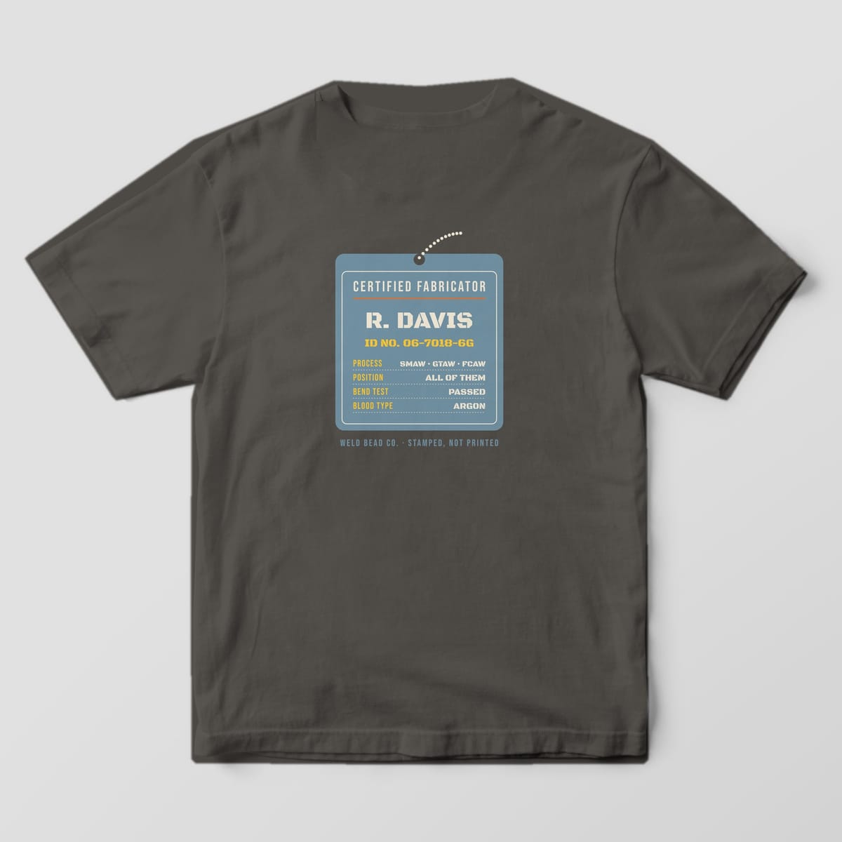 Back print on a Pepper Comfort Colors 1717 tee: A hanging steel ID tag: "Certified Fabricator", the custom name, ID number and a spec list (process, position, bend test, blood type: argon)