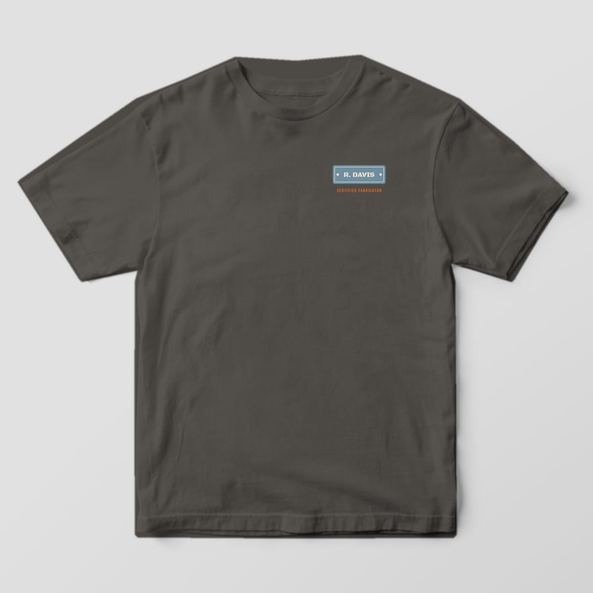 Front of the Pepper Comfort Colors 1717 tee showing the left-chest print: Small left-chest steel nameplate with the custom name and "Certified Fabricator" below