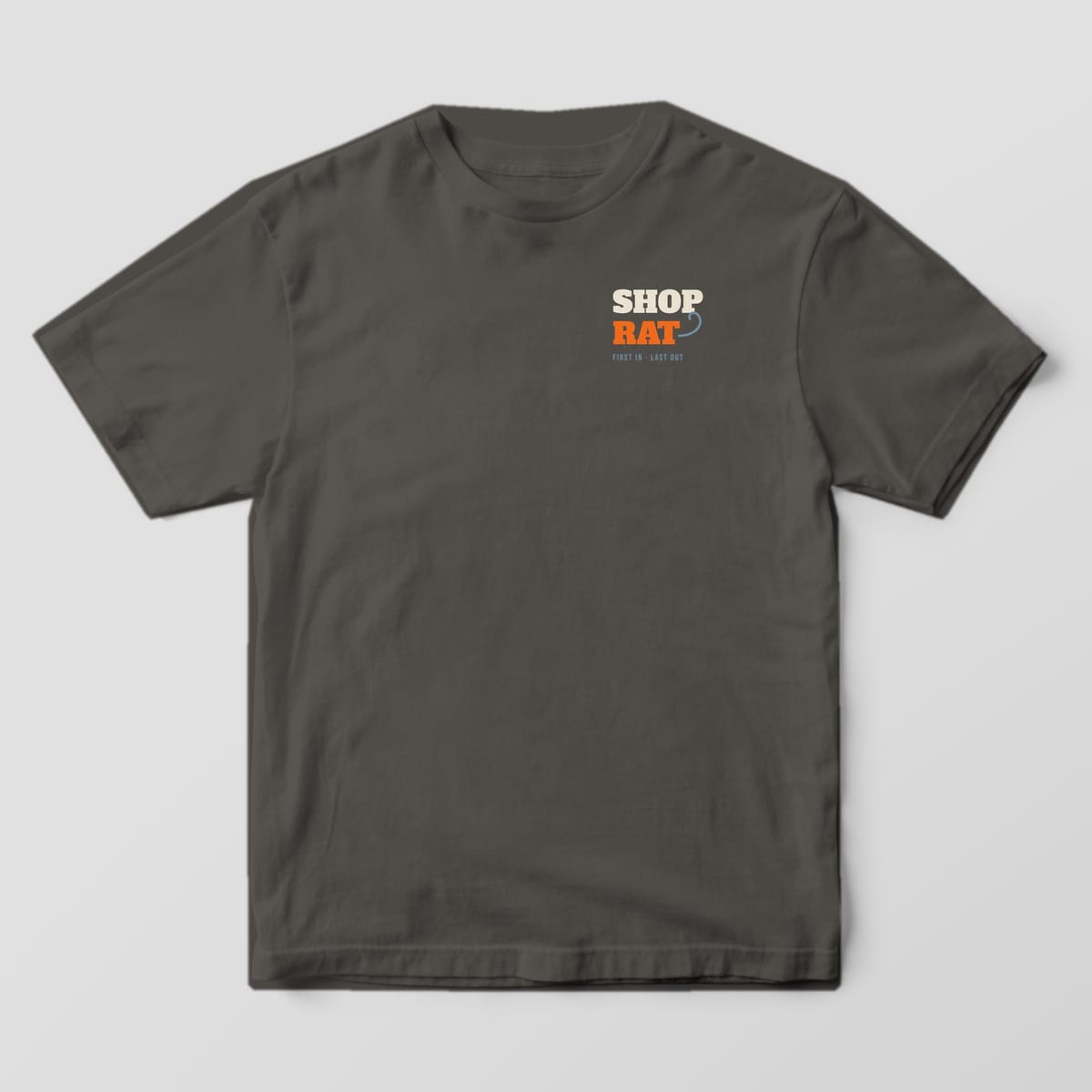 Front of the Pepper Comfort Colors 1717 tee showing the left-chest print: Left-chest "Shop Rat" slab type with a curling rat tail and "First In · Last Out"