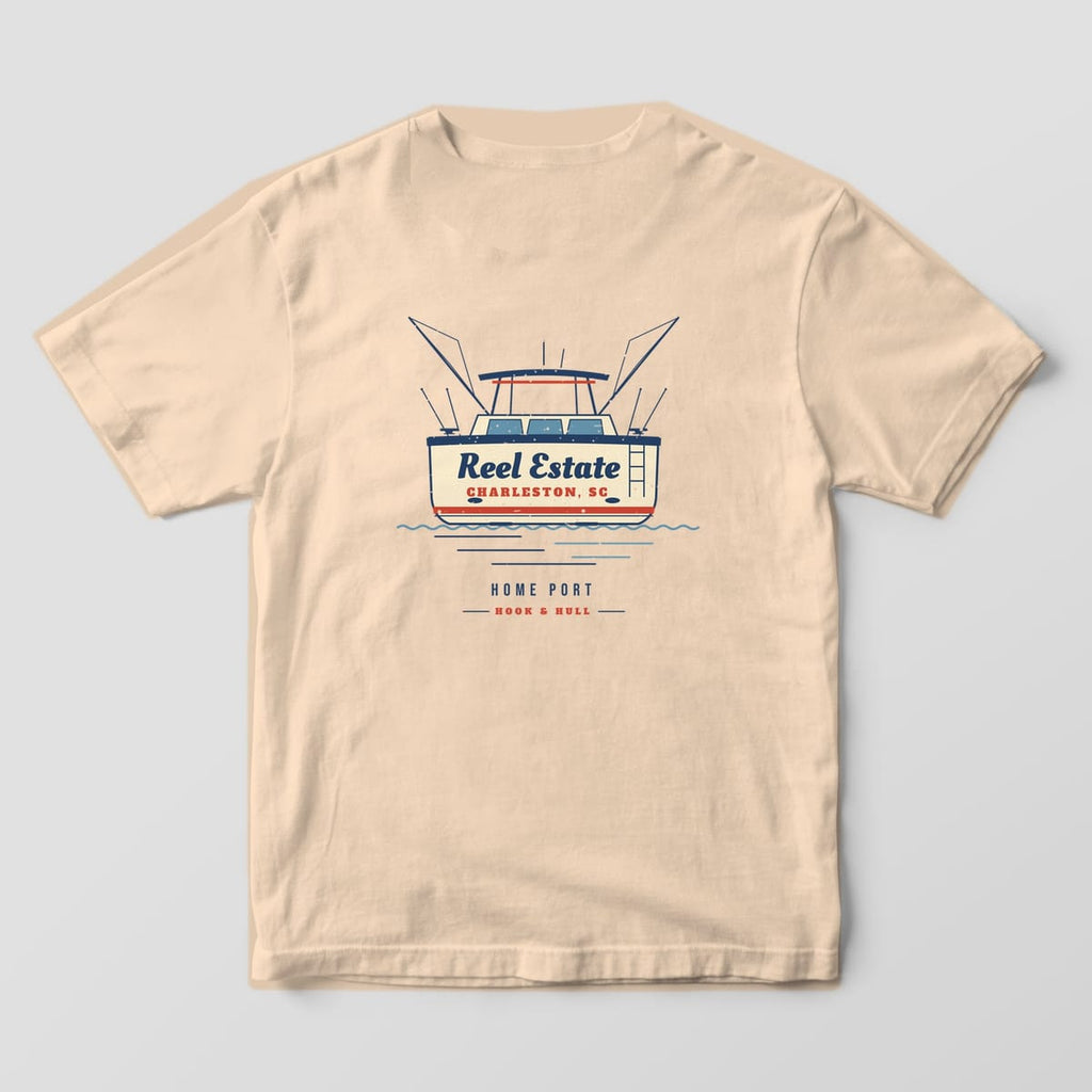 Back of an ivory Comfort Colors 1717 T-shirt showing the stern view of a sportfishing boat with outriggers and the name Reel Estate, Charleston SC lettered on the transom
