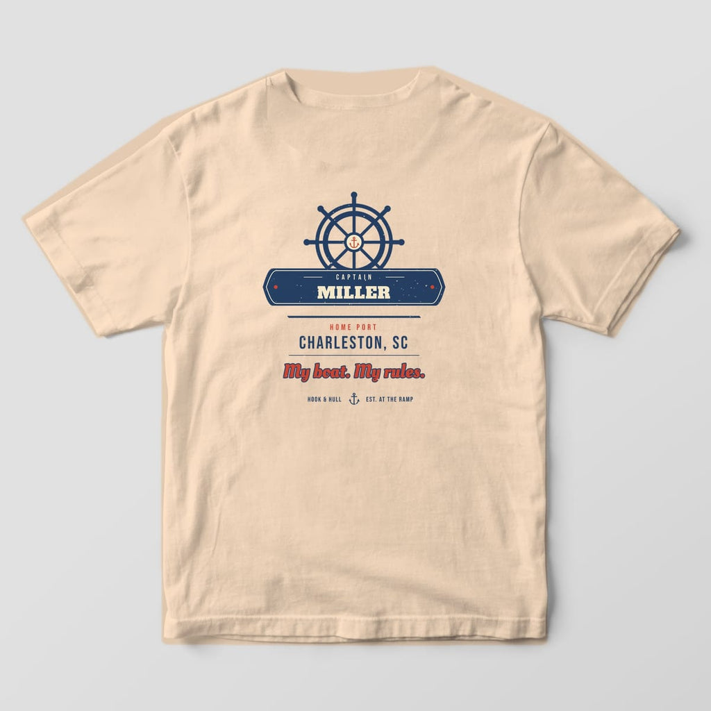 Back of an ivory Comfort Colors 1717 T-shirt showing a ship's wheel over a navy nameplate reading Captain Miller, home port Charleston SC and the line My boat. My rules