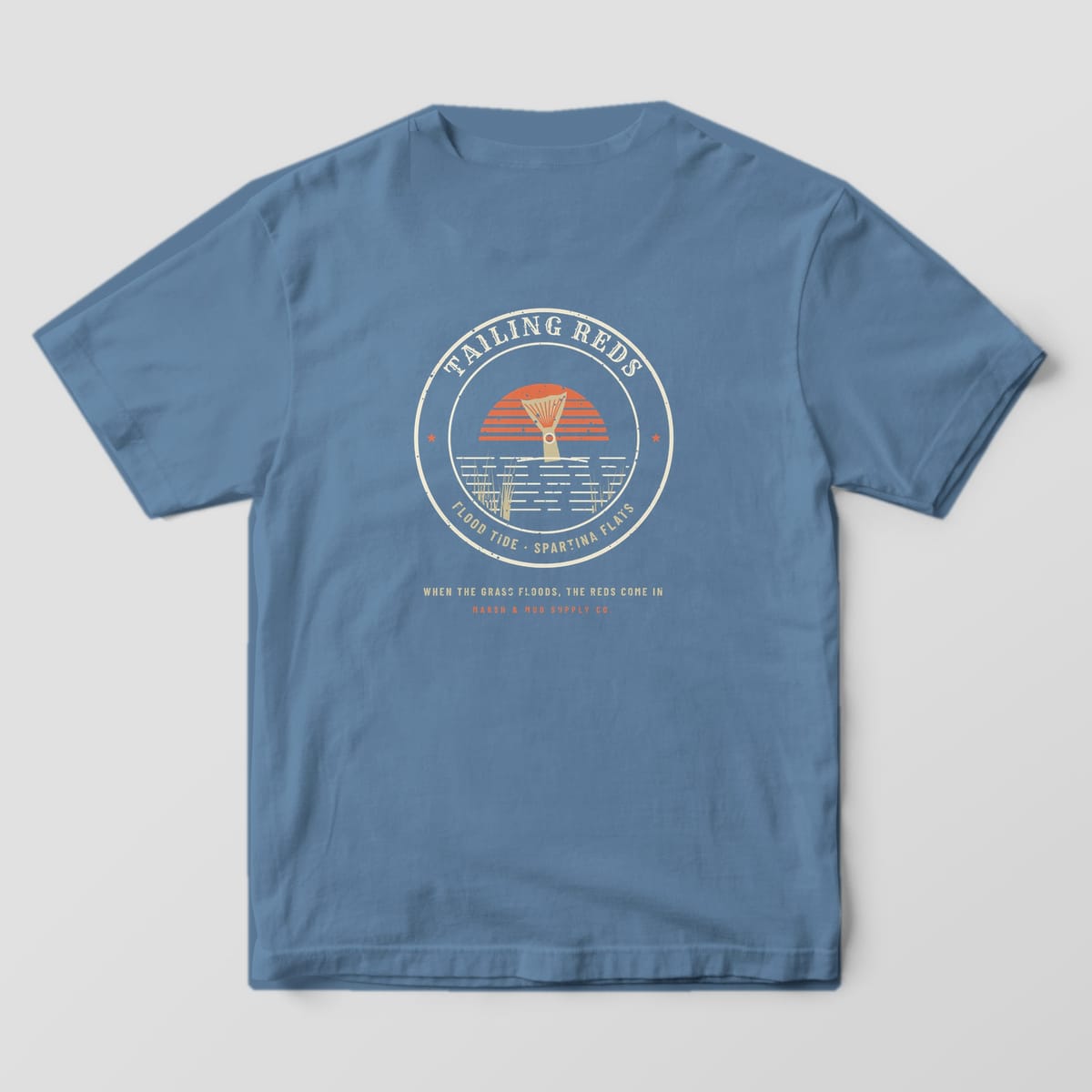 Back of a blue jean Comfort Colors 1717 tee with a cream badge showing a redfish tail in flooded marsh grass