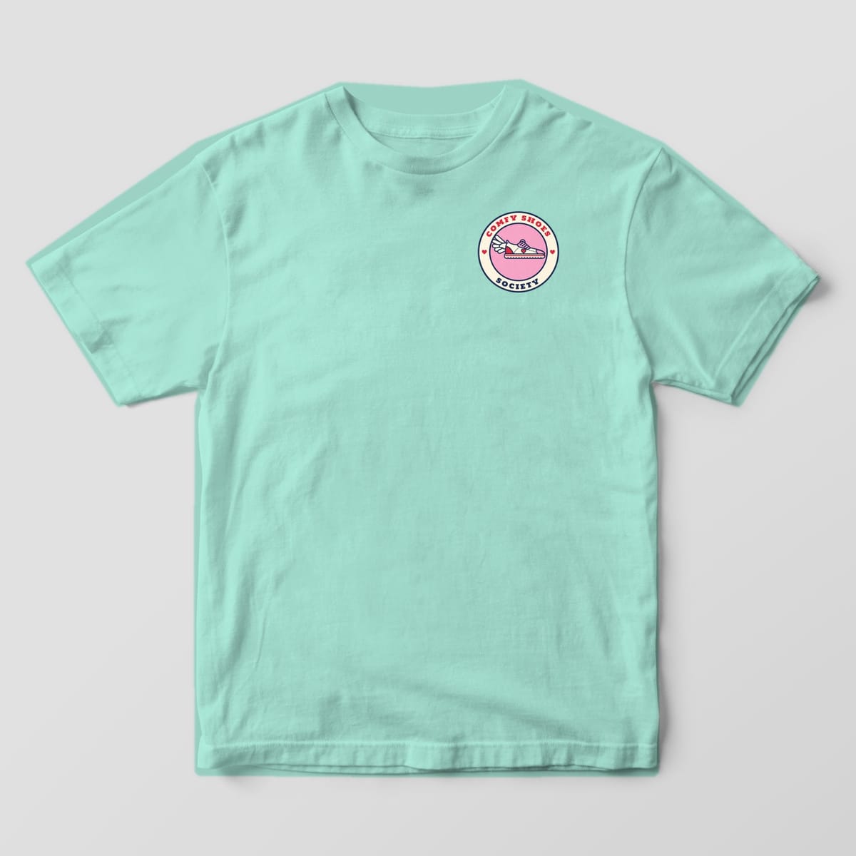 Front of a chalky mint Comfort Colors 1717 tee with a small winged sneaker badge on the left chest