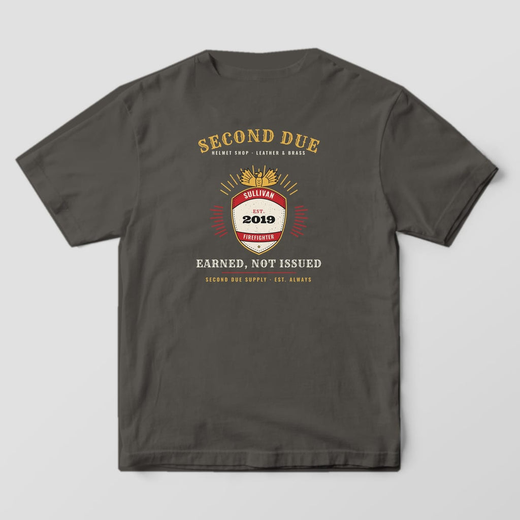 Back of a pepper Comfort Colors tee with a fire helmet frontpiece, brass eagle, custom name SULLIVAN, EST. 2019 and Earned, Not Issued