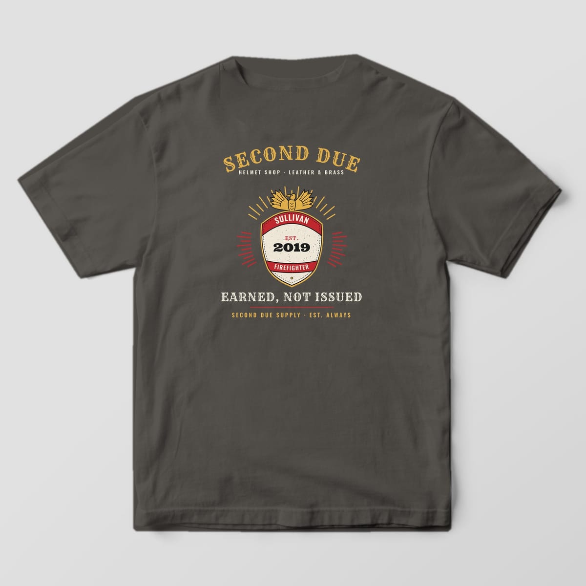 Back of a pepper Comfort Colors tee with a fire helmet frontpiece, brass eagle, custom name SULLIVAN, EST. 2019 and Earned, Not Issued