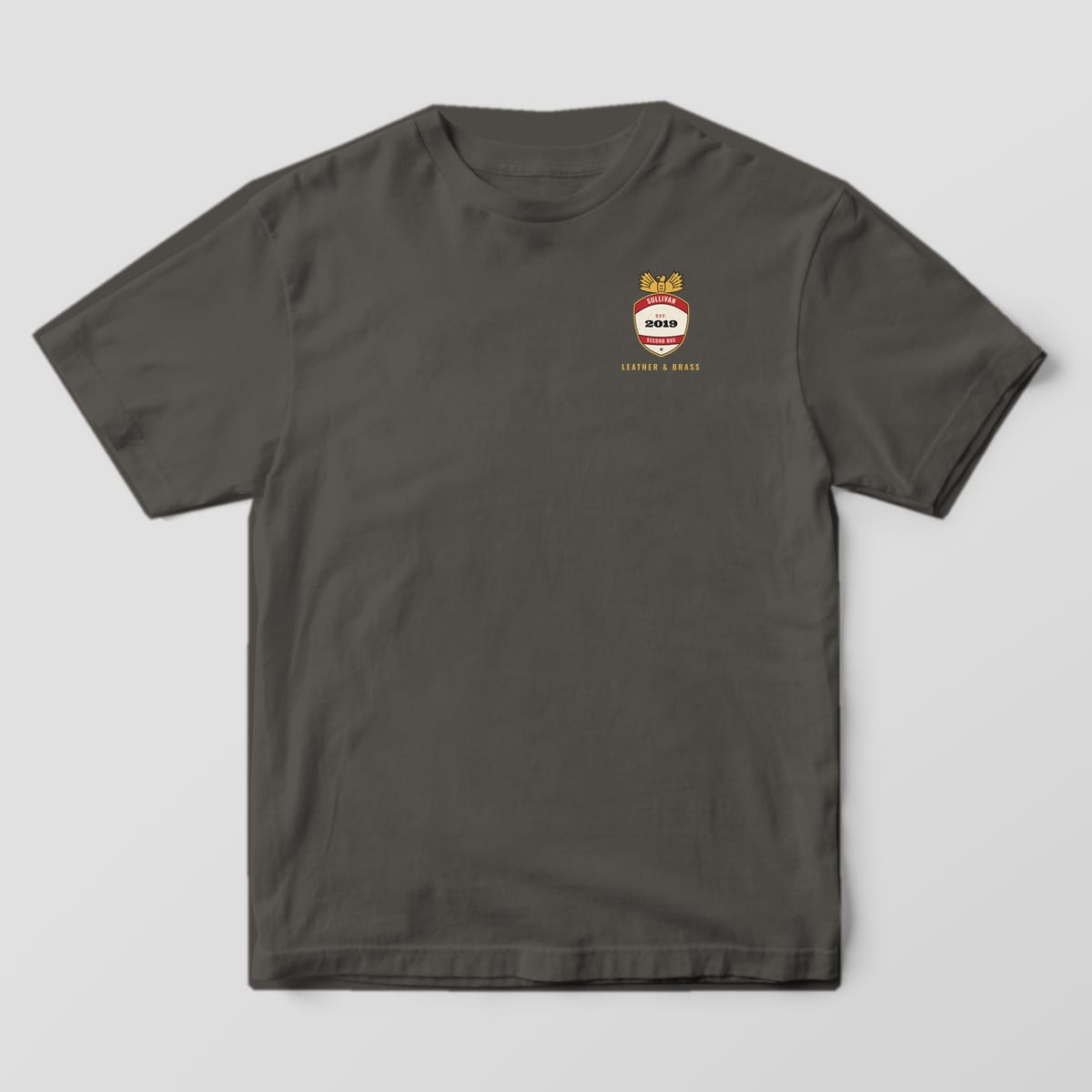 Front of a pepper Comfort Colors tee with a small personalized helmet shield and Leather & Brass on the left chest