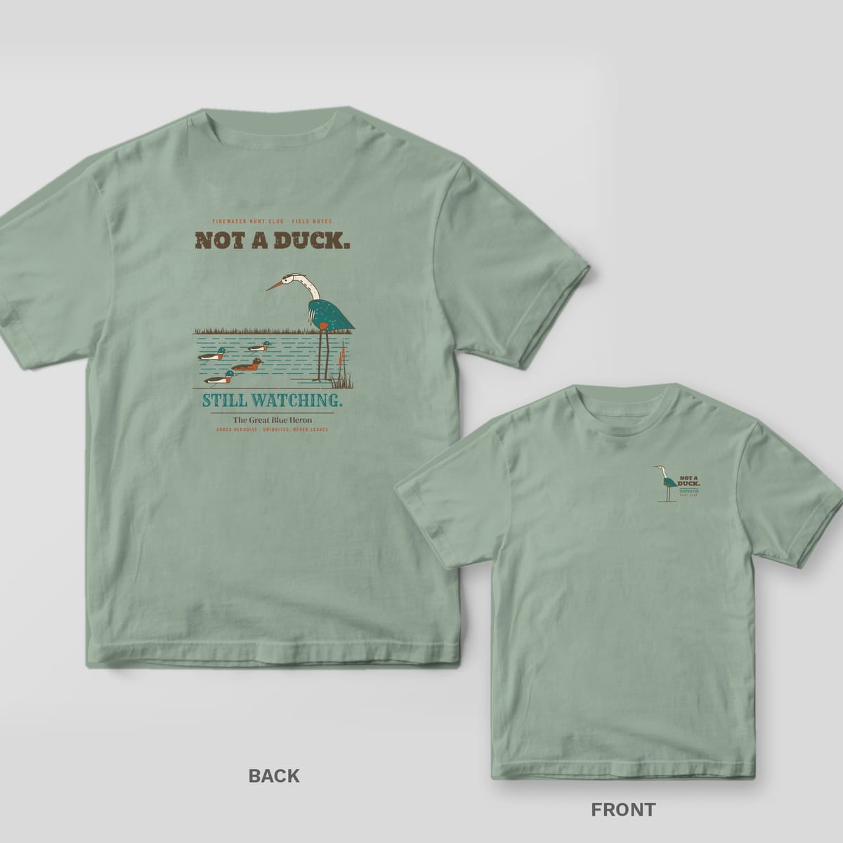 Back and front views of a sage green T-shirt with a heron eyeing duck decoys on the back and a small heron on the chest
