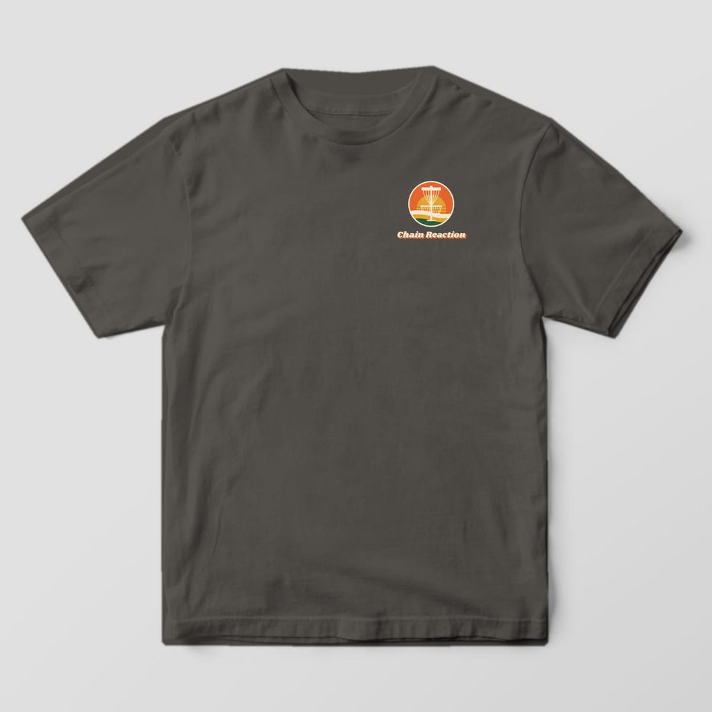 Front of a Pepper Comfort Colors 1717 tee with a small sunset badge and Chain Reaction wordmark on the left chest.