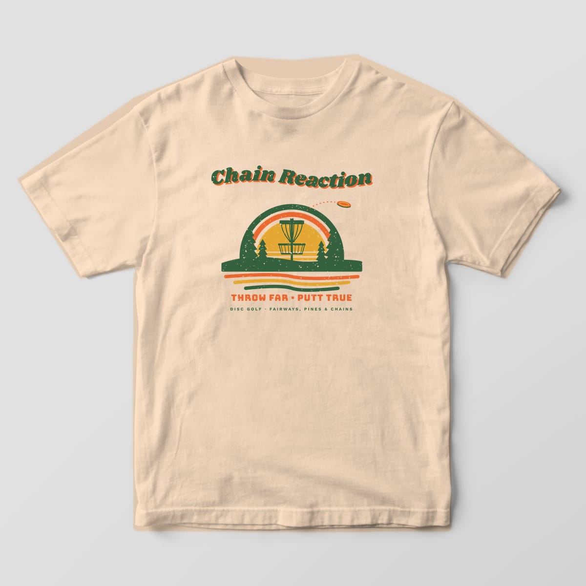 Front of an Ivory Comfort Colors 1717 tee with a full-front retro sunset with a disc golf basket, pines and rainbow arch under wavy Chain Reaction lettering.