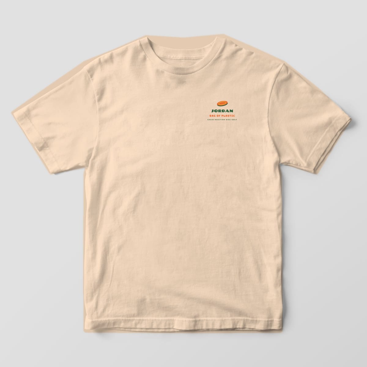 Front of an Ivory Comfort Colors 1717 tee with a small disc icon with a custom name and Bag of Plastic text on the left chest.