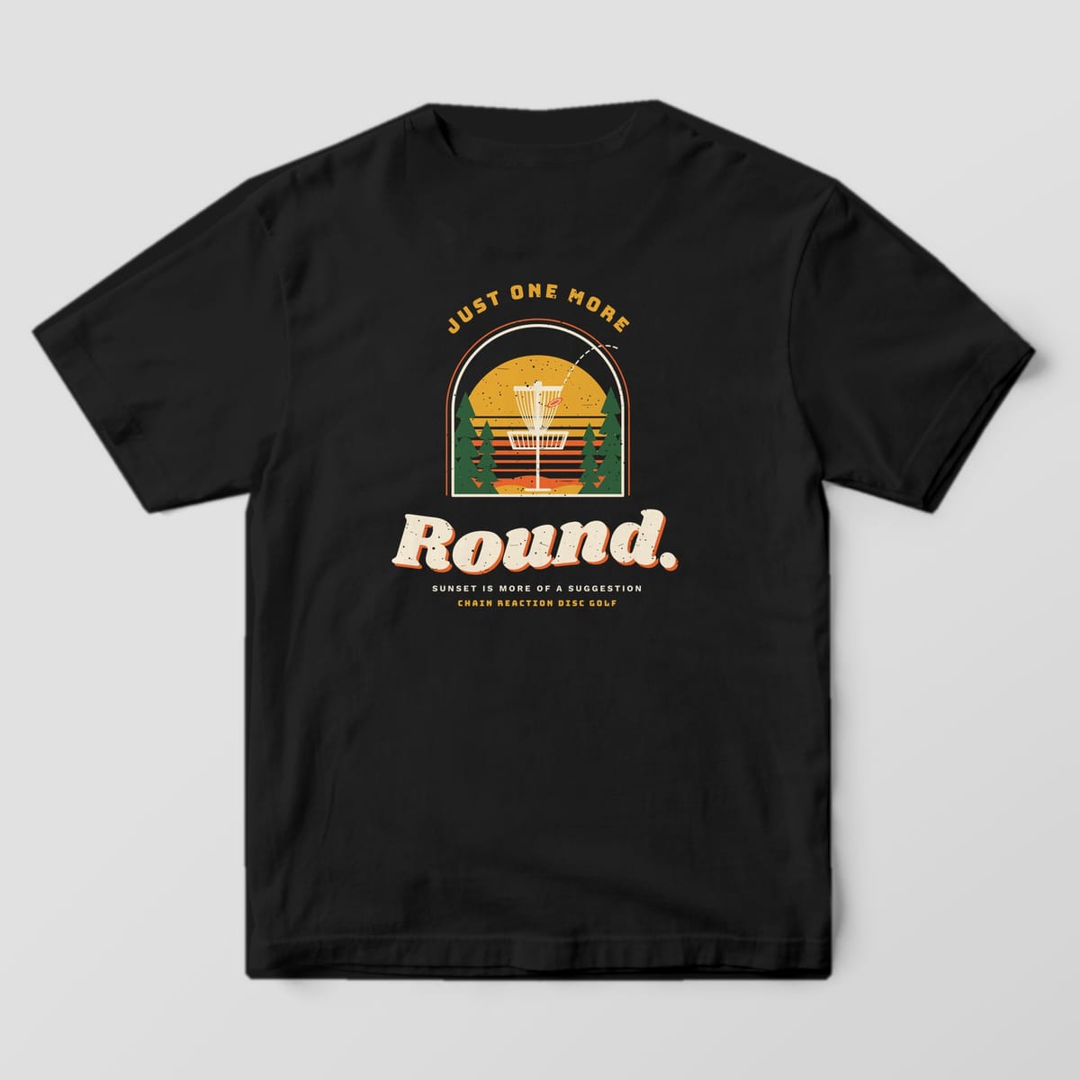 Back of a black Comfort Colors t-shirt with a disc golf basket in front of a striped sunset and the words Just One More Round