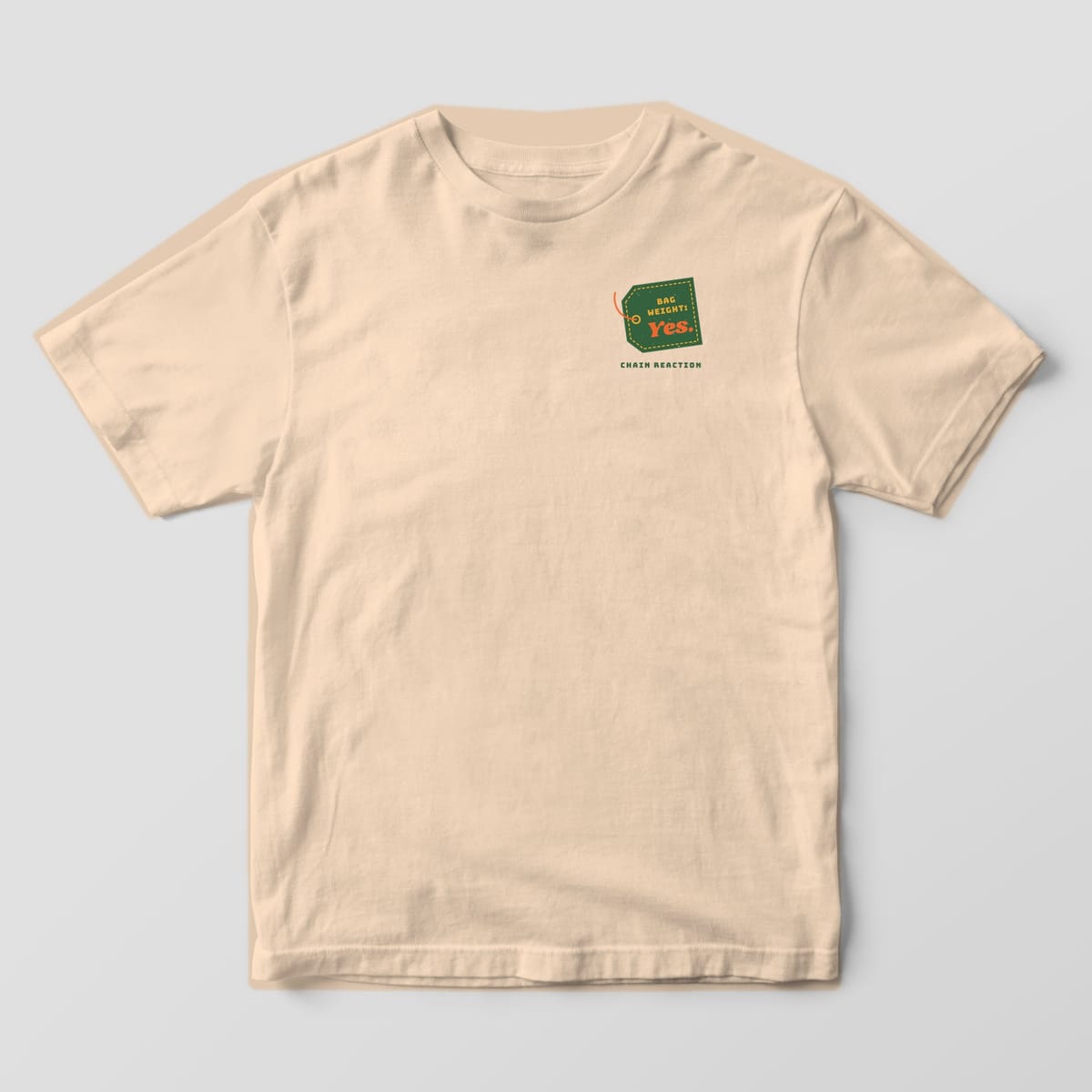 Front of an ivory Comfort Colors t-shirt with a small green luggage tag reading Bag Weight: Yes