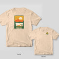 Ivory t-shirt shown back and front: vintage poster with orange mountains, cream sun, green pines and a winding fairway to a basket, Walk Your Course title, basket badge on chest