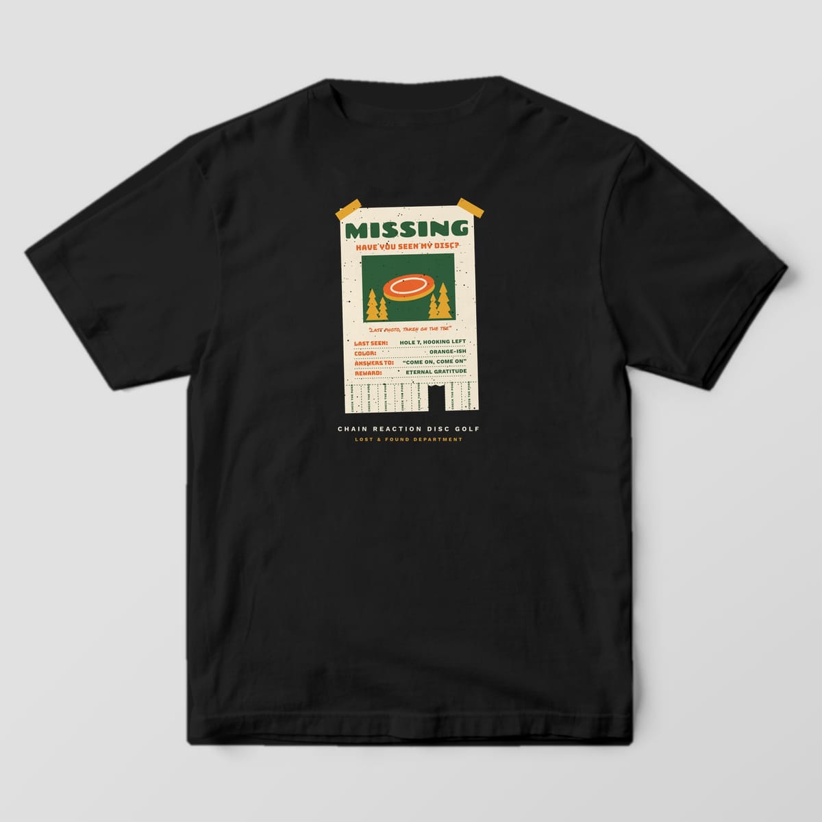Back of a Black Comfort Colors 1717 tee printed with a cream taped-up Missing poster with a photo of an orange disc, lost-disc details and tear-off tabs.