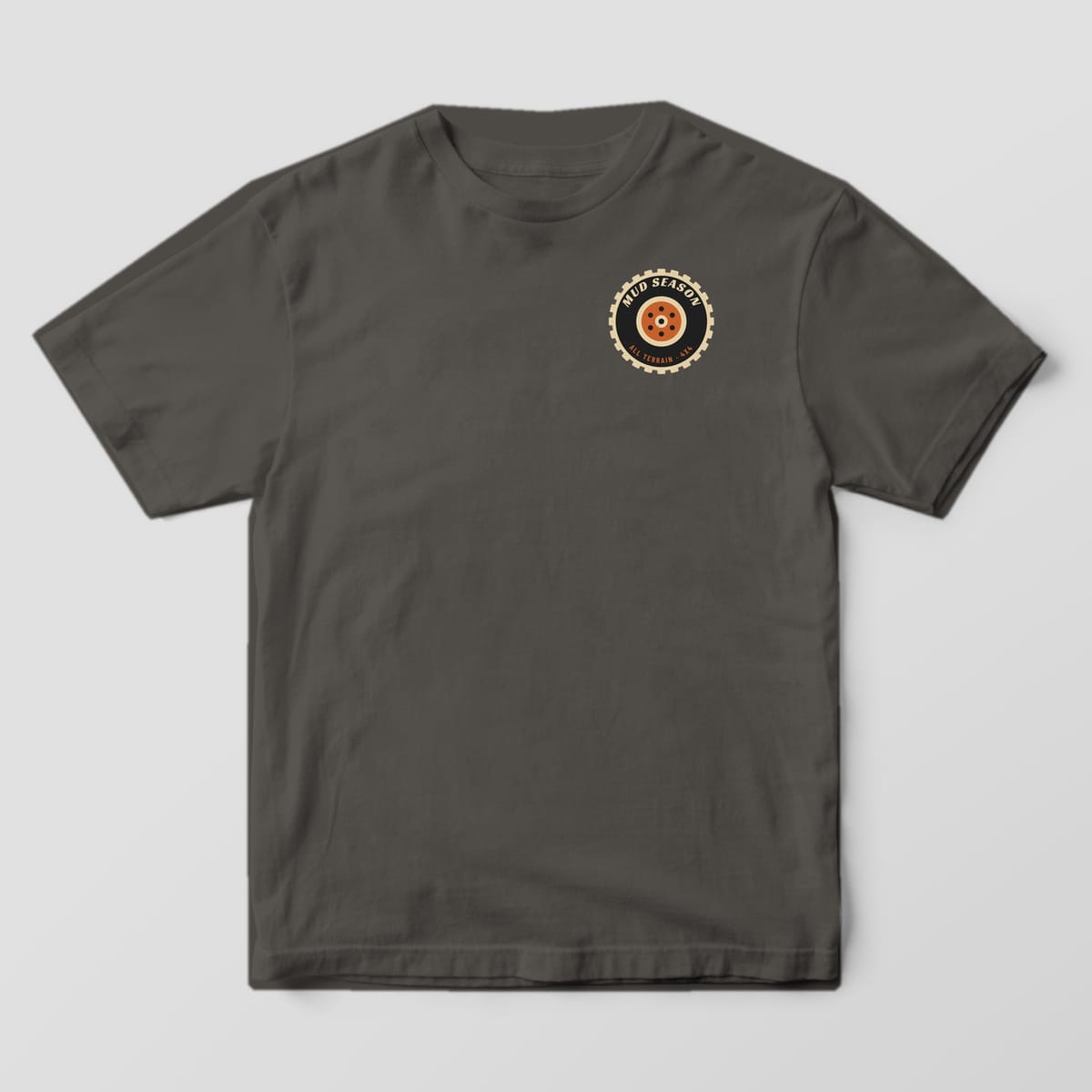 Front of a Pepper Comfort Colors 1717 tee with a small left-chest tire badge with Mud Season lettering