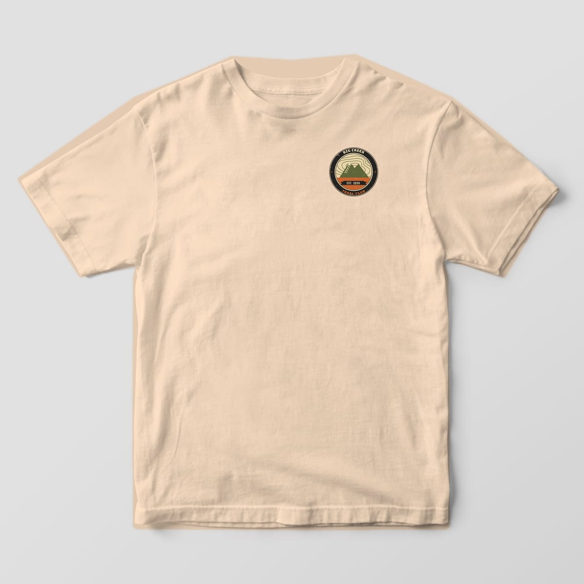 Front of an ivory Comfort Colors 1717 T-shirt with a small personalized trail club badge on the left chest.