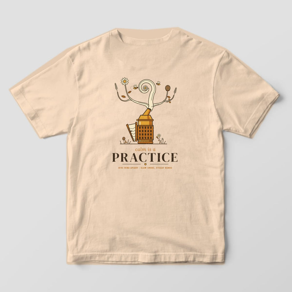 Back of a ivory Comfort Colors 1717 T-shirt printed with a vintage bee smoker whose smoke curls into wildflowers above the words calm is a practice.