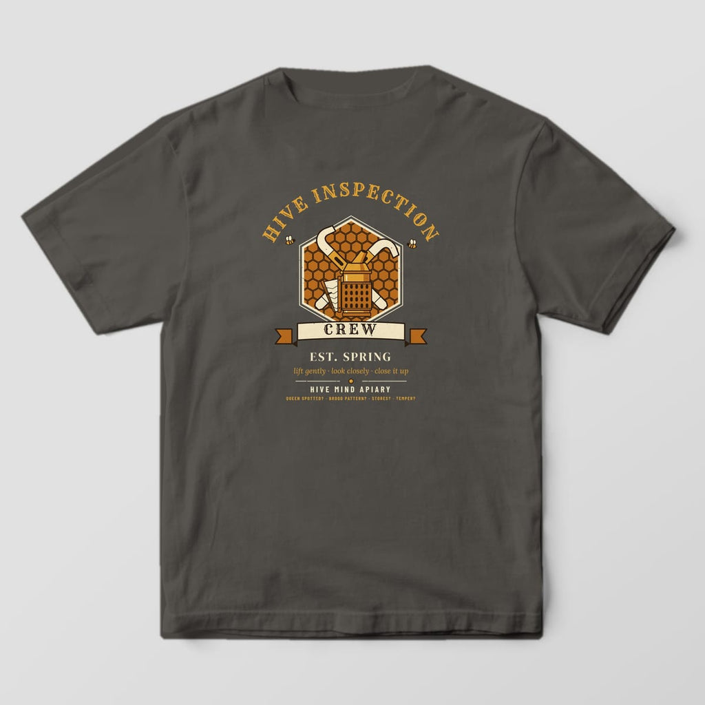 Back of a pepper Comfort Colors 1717 T-shirt printed with a crest of crossed hive tools and a bee smoker on a honeycomb hexagon titled Hive Inspection Crew.
