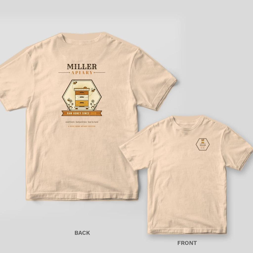 Back and front of an ivory Comfort Colors T-shirt; the back shows a personalized hexagon emblem with the name Miller Apiary, a painted beehive and a Raw Honey Since 2019 banner, the front has a small hexagon Miller Apiary badge on the left chest.