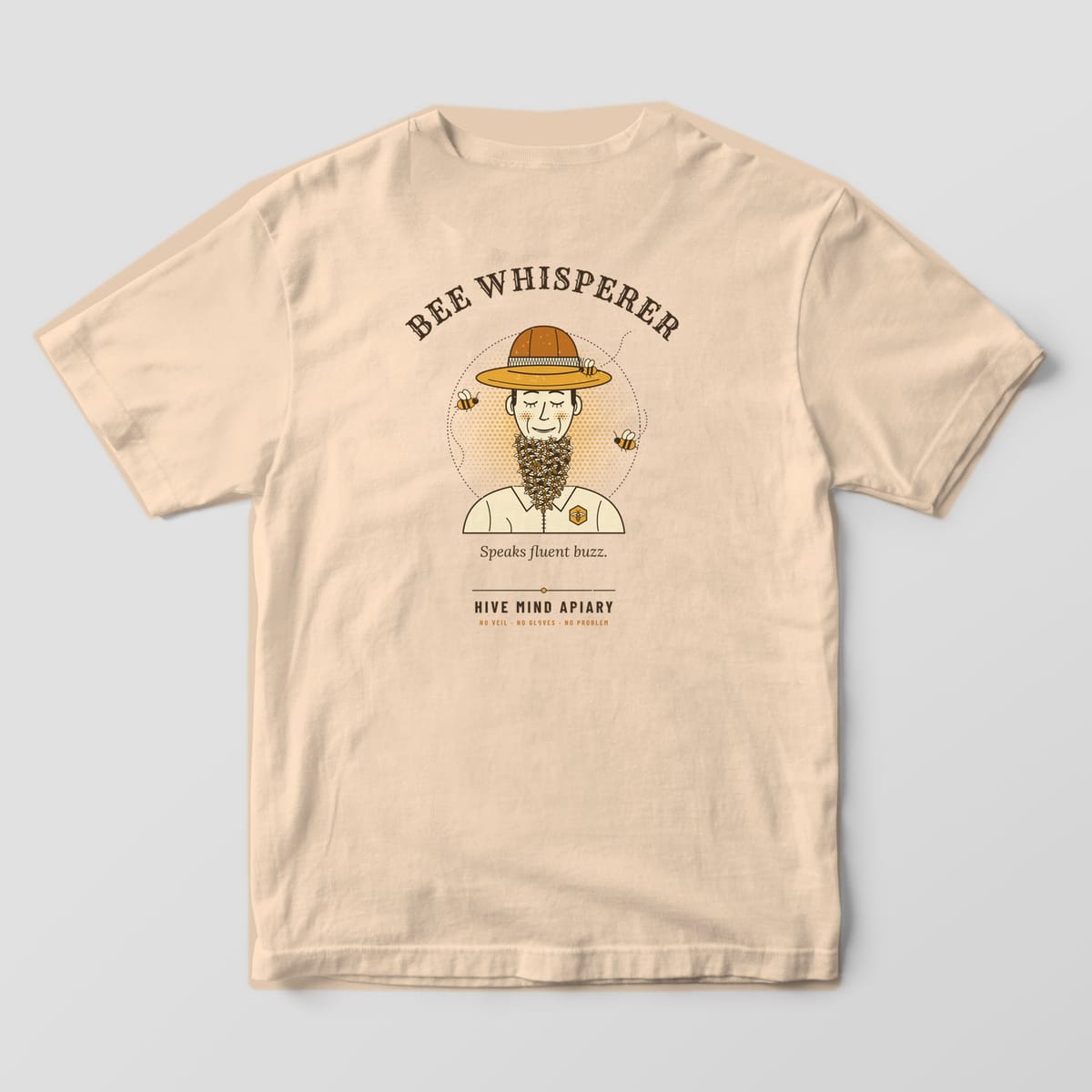 Back of an ivory Comfort Colors 1717 T-shirt printed with a retro portrait of a smiling beekeeper with a beard made of bees, titled Bee Whisperer.