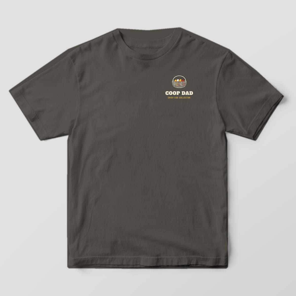 Front of a pepper Comfort Colors 1717 tee with a small wire egg basket and Coop Dad text on the left chest.